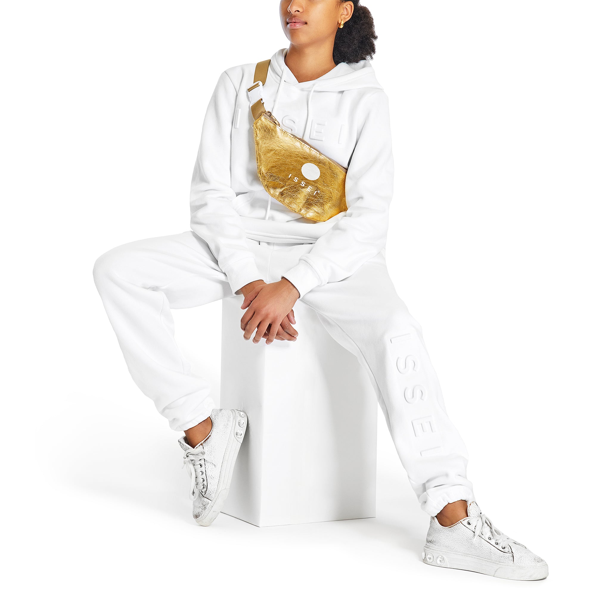 Person wearing a white Issei hoodie and sweat pants with a gold fanny pack on a white background
