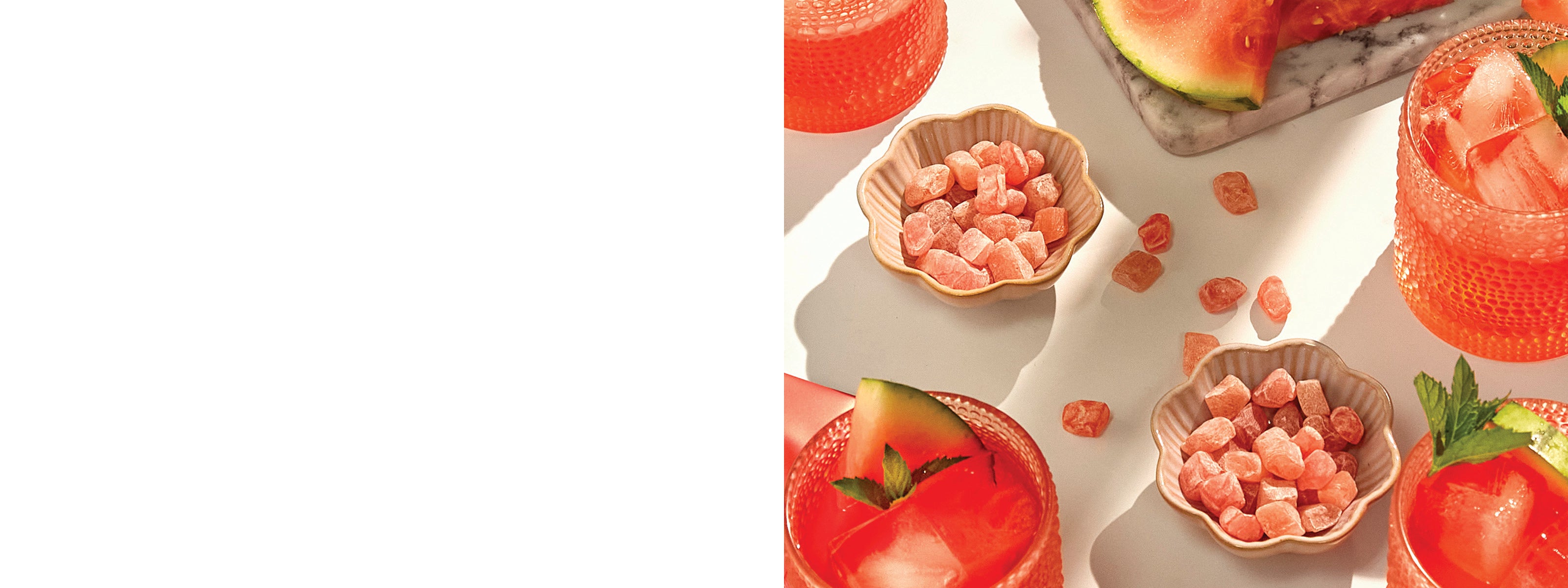 Mochi gummy candies presented in small beige scalloped bowls, with watermelon slices and pink drinks arranged around them on a bright white surface.