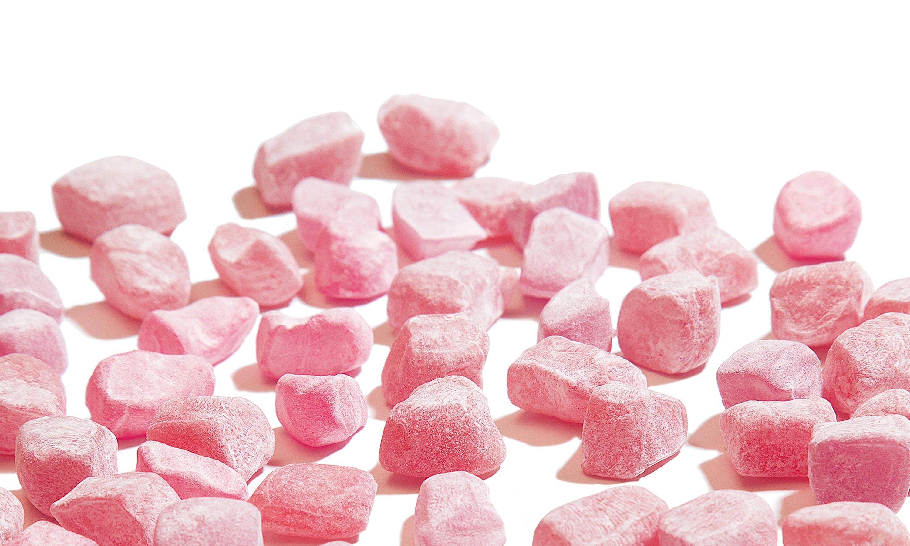 Pink mochi gummies scattered on a white background