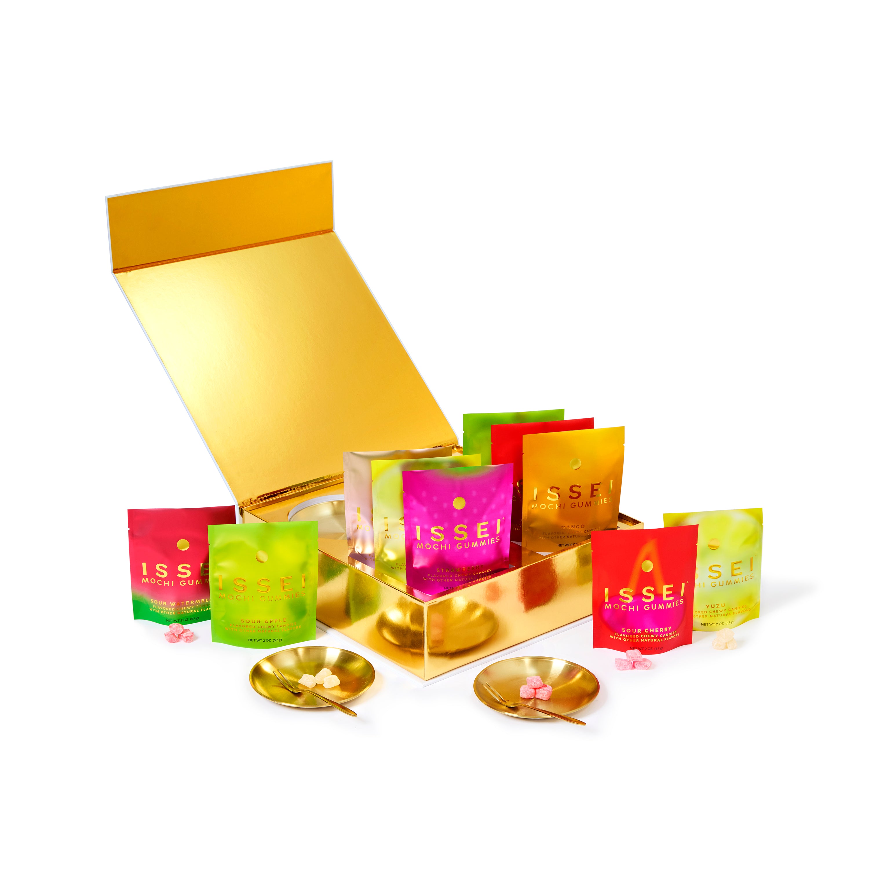 Assorted colorful Issei Mochi Gummies bags in a gold box with gold plates and forks on a white background