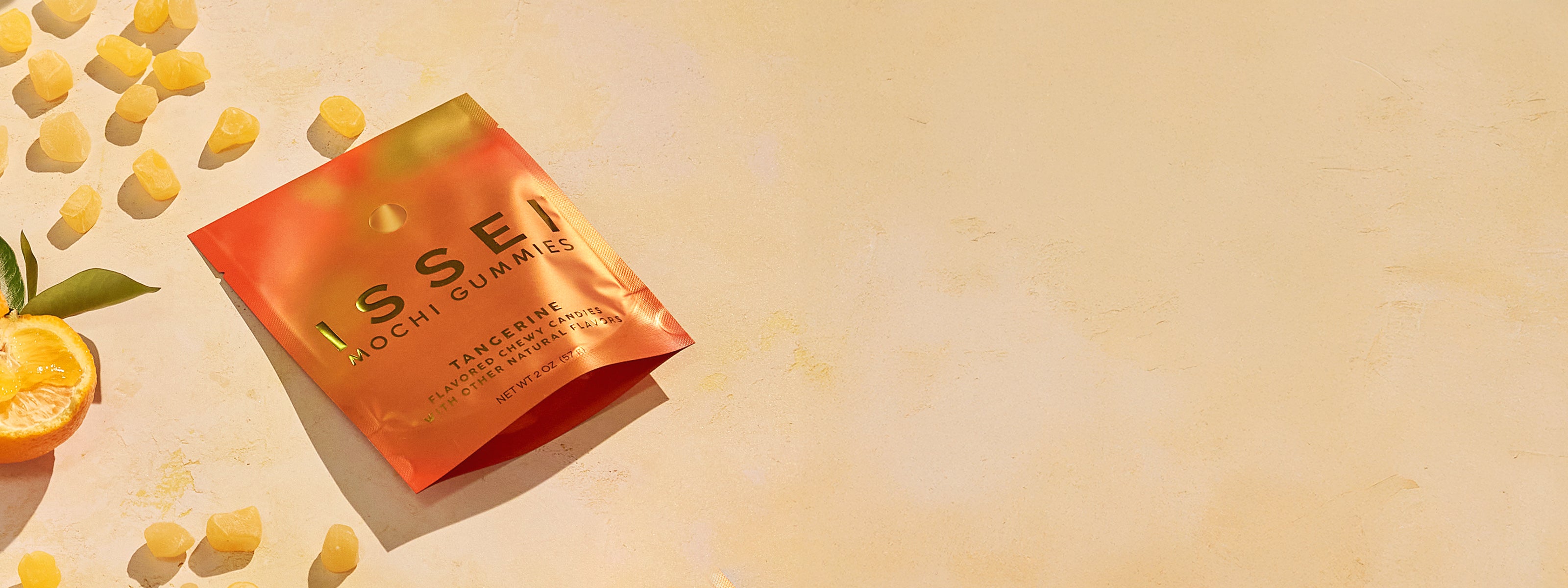 Issei Mochi Gummies tangerine bag pictured with gummies and a cut tangerine on a textured background
