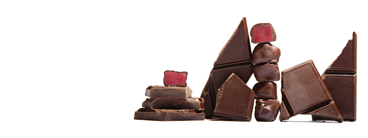 A stack of Dark Chocolate Covered Mochi Gummies surrounded by pieces of chocolate bars on a white background